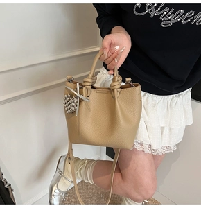 Detail of khaki lychee grain leather bucket bag featuring a unique knotted handle and heart charm