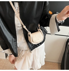Mini cream saddle bag with teddy bear embossing worn by a model in a casual setting