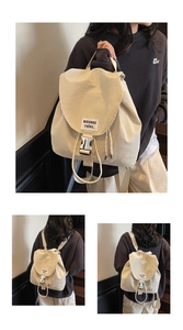 Close-up of beige drawstring backpack showing silver metal buckles and woven label detail