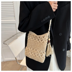 Detail of hollow-out straw phone bag featuring boho tassels and wooden bead accents