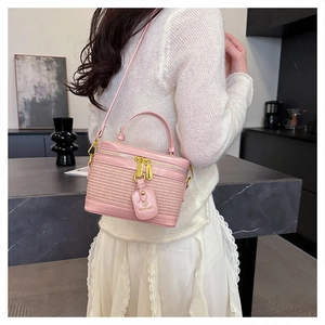 Detailed view of pink woven crossbody bag with gold zippers and brand letter tag