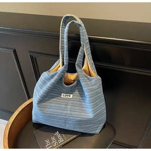 Detail of blue striped tote bag featuring LOVE patch and magnetic clasp on wooden stool