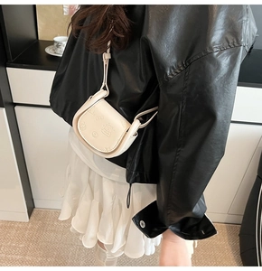 Detail of cream saddle bag with embossed bear and bow patterns on model's outfit