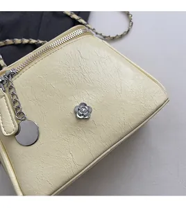 Détail du sac bandoulière crème avec texture grainée et logo floral camélia argenté