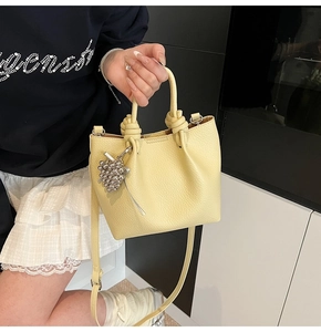 Close-up of vibrant yellow lychee leather bucket bag with knot handle and silver charm