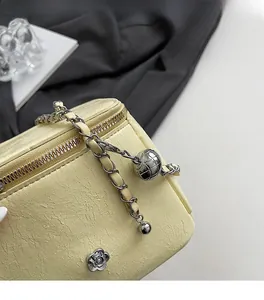 Gros plan du sac en cuir crème avec boucle camélia argentée et bandoulière en chaîne