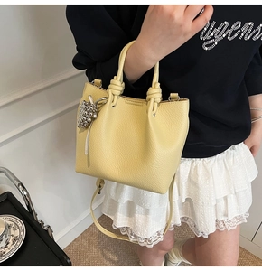 Detail of light yellow lychee grain bucket bag with knot handle and grape pendant