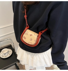 Detailed close-up of a mini saddle crossbody bag with red trim and cartoon bear prints