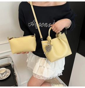 Detail of bright yellow bucket bag with lychee texture and knot handle with silver charms