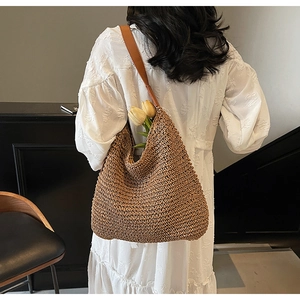 Close-up of woven straw shoulder bag with brown leather strap and bohemian details