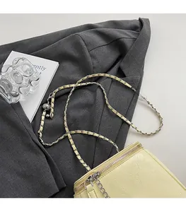 Gros plan détaillé du sac bandoulière jaune pâle avec chaîne en argent sur tissu gris