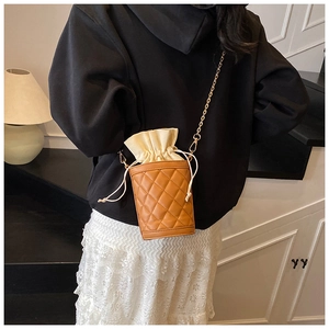 Detail of quilted brown bucket bag with beige drawstring lining and gold chain strap