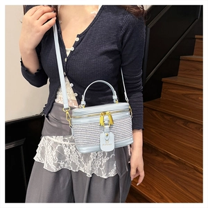 Detailed close-up of light blue cylindrical vanity bag with woven texture and gold zippers