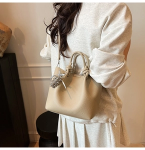 Detail of apricot pebbled leather bucket bag featuring a silver bead charm and thin strap