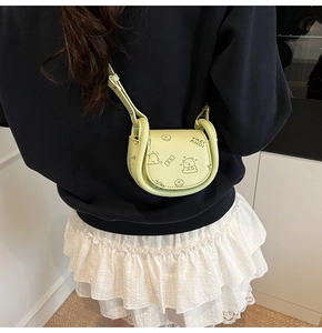 Detail of mint green saddle bag with cartoon graphics worn by a model in casual setting