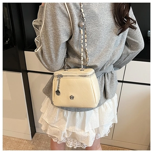 Détail d'un sac boîte en cuir crème avec logo fleuri et chaîne argentée sur modèle