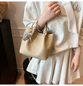 Detail of beige bucket bag with knotted handle and silver grape charm in a lifestyle view