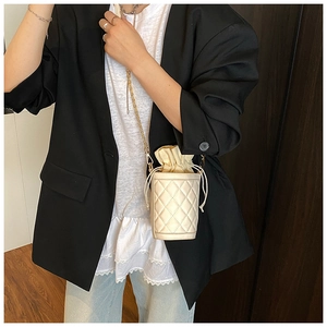 Close-up of beige quilted bucket bag with drawstring closure and gold chain strap