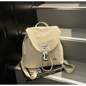 Detail of light beige nylon bucket backpack featuring metallic buckles and drawstring closure