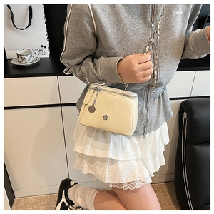 Detail of a creamy white crossbody bag with metal flower logo and woven chain strap