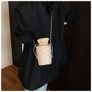 Detail of beige quilted bucket bag with chain strap and drawstring closure on a model