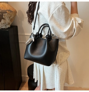 Detail of black litchi grain leather bucket bag with metal bead pendant and shoulder strap