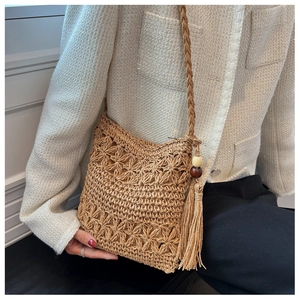 Close-up of hand-woven hollow straw shoulder bag with long tassels and wood beads