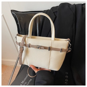 Dettaglio borsa tote color crema con trama litchi e cinturini marroni su sedia nera