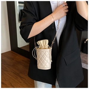 Quilted cream bucket bag with drawstring closure and golden chain strap on a model