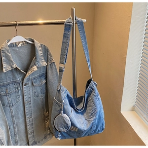 Detail of blue washed denim tote bag featuring adjustable strap and round coin purse charm