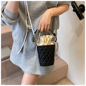 Detail of black quilted bucket bag with cream drawstring liner and gold chain strap
