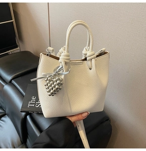 Detailed shot of white lychee leather bucket bag with silver ball charm and knot handle