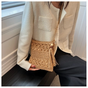 Detailed close-up of straw woven crossbody bag with hollow patterns and long tassels