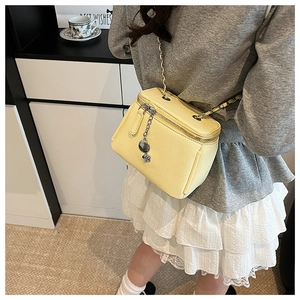 Detail view of a bright yellow box-shaped crossbody bag with gold chain strap on model