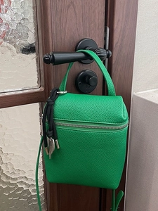 Bright green lychee grain leather crossbody bag hanging on a vintage dark wood door handle