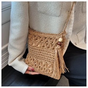 Detail of hollow floral woven straw bag with decorative long tassels and wood beads