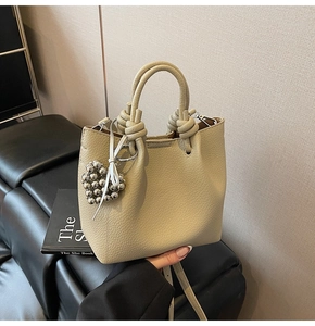 Detail of beige bucket bag featuring a woven knotted handle and silver heart charm