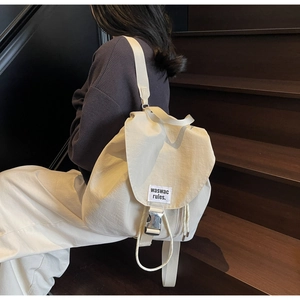 Detail of a minimalist cream nylon backpack featuring a metal buckle and woven brand label