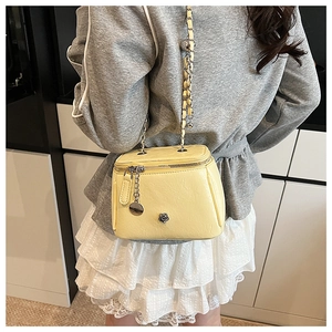 Detail of yellow crossbody bag with metal rose emblem and woven chain strap on model