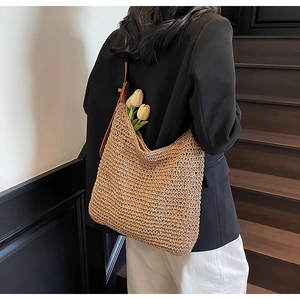Detail of a large woven straw shoulder bag in oatmeal color worn on a minimal staircase