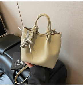 Detail view of beige lychee leather bucket bag with knot handle and grape bead charm
