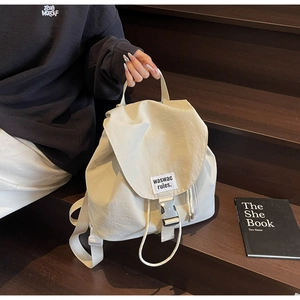 Detail view of cream drawstring bucket backpack with buckle on wooden stairs with book