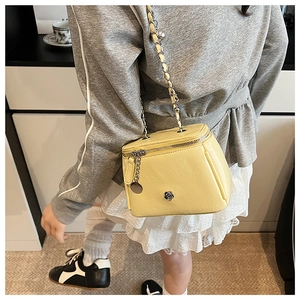 Detail view of yellow box-shaped crossbody bag with chain strap and flower charm on a model