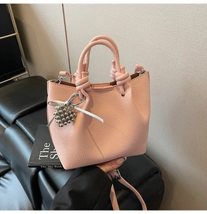 Detail of pink lychee leather handbag with knotted handle and silver beaded charm