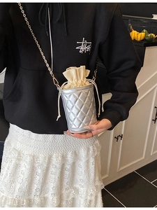 Silver quilted drawstring bucket bag with metal chain strap worn by a model