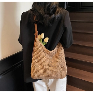 Detail of handwoven straw tote featuring a brown faux leather strap and large capacity