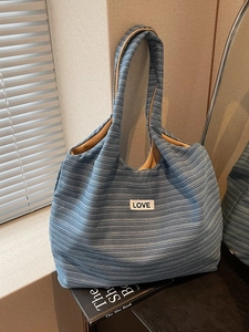 Blue and white striped canvas tote bag with Love patch leaning against a wall
