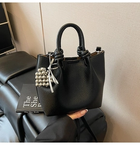Detail of black lychee grain leather handbag with knotted handle and silver bead charm