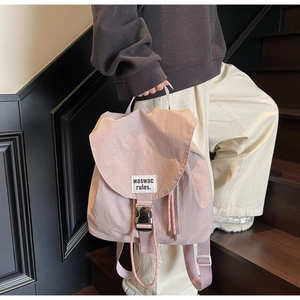 Detail of light pink nylon drawstring backpack featuring a silver buckle and letter patch