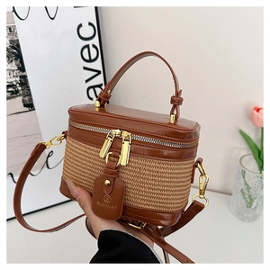 Detail of a brown leather and woven straw box bag featuring gold hardware and logo tag